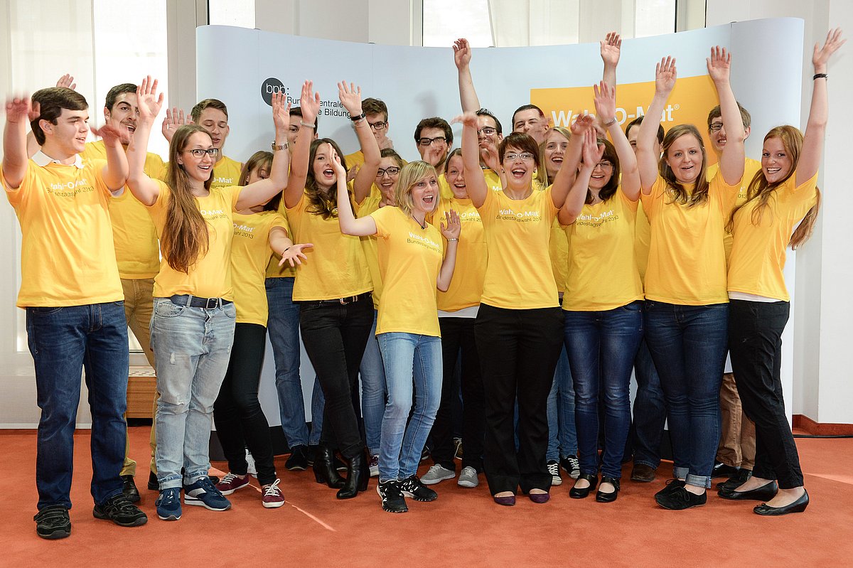 Der Teilnehmende der Jugendredaktion des Wahl-O-Mat in gelben T-Shirts heben die Hände.