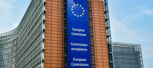 Das Gebäude der Europäischen Kommission in Brüssel mit stahlgrauer Front und blauem EU-Banner.