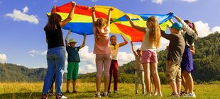 Eine Gruppe Kinder und eine erwachsene Person spielen in der Natur mit einem Fallschirm-Schwungtuch