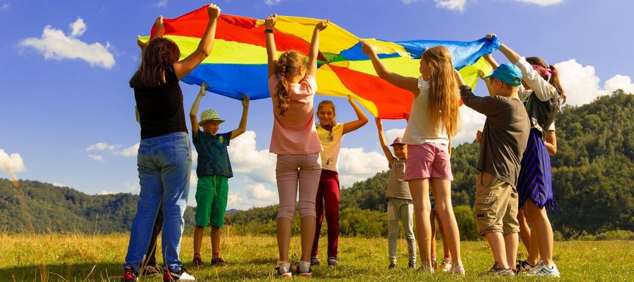 Eine Gruppe Kinder und eine erwachsene Person spielen in der Natur mit einem Fallschirm-Schwungtuch