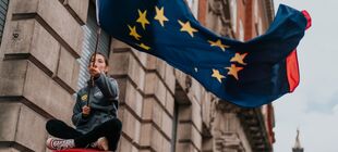Eine junge Frau schwenkt eine große Europaflagge, im Hintergrund ist ein Gebäude zu sehen