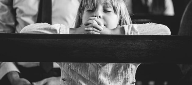 Ein Kind kniet an einer Holzbank und betet