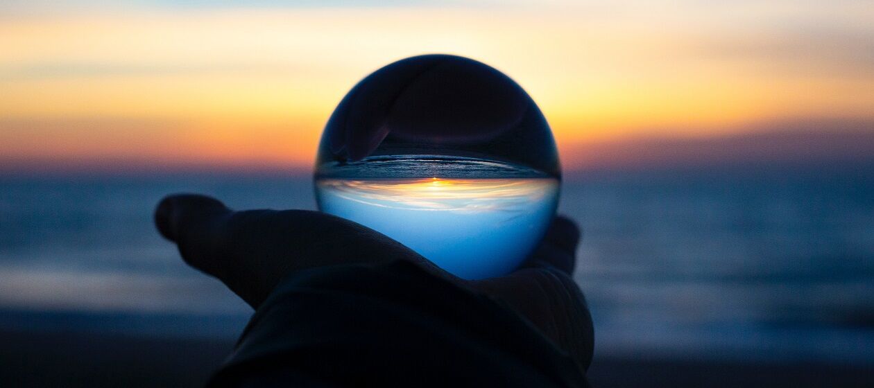 In einer Glaskugel spiegelt sich der Sonnenuntergang über dem Meer