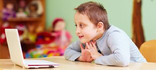 Ein Junge mit Behinderung sitzt in einem Klassenraum und schaut auf einen Laptop