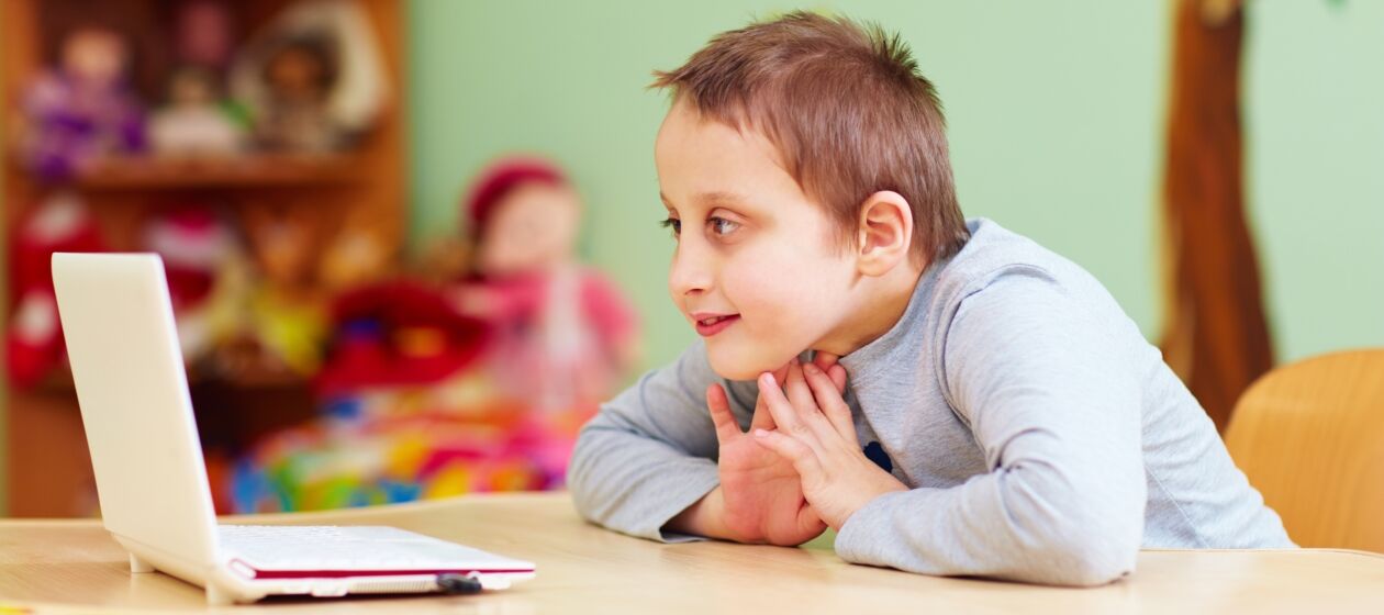 Ein Junge mit Behinderung sitzt in einem Klassenraum und schaut auf einen Laptop