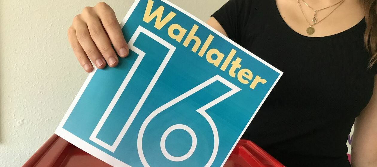 Eine Jugendliche hät einen blauen Flyer mit der Aufschrift "Wahlalter 16"