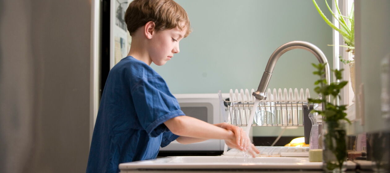 Ein Junge im Grundschulalter wäscht sich in der Küche die Hände