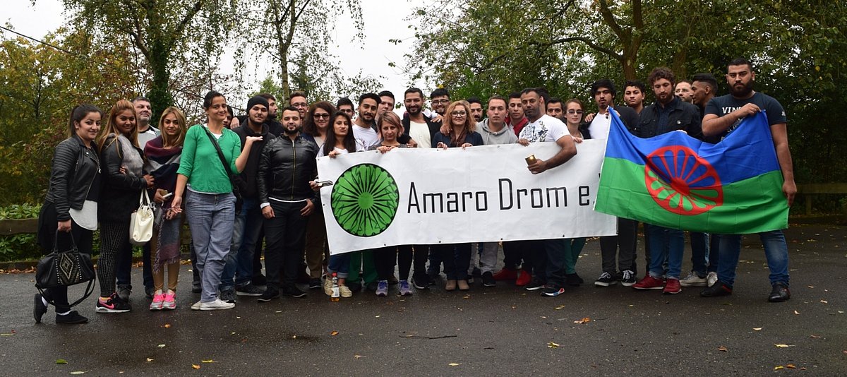 Eie Gruppe von Teilnehmern die ein Banner von Amaro Drom e.V. hält
