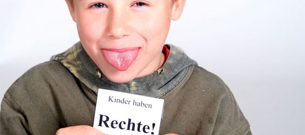 Ein Junge streckt die Zunge raus und hält ein Schild in der Hand "Kinder haben Rechte!"