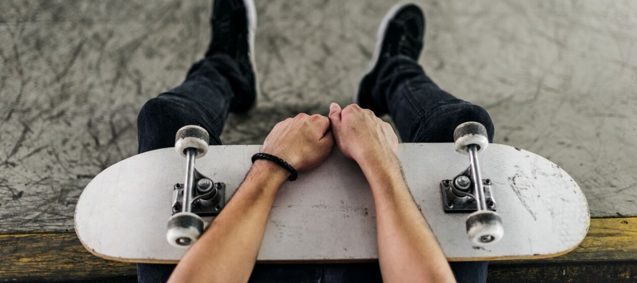 Sitzender Jugendlicher von oben mit Skateboard auf dem Schoß