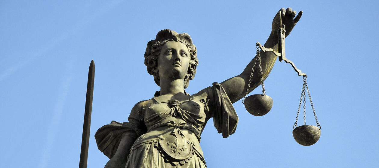 Statue der Gerechtigkeitsgöttin Justitia vor blauem Himmel