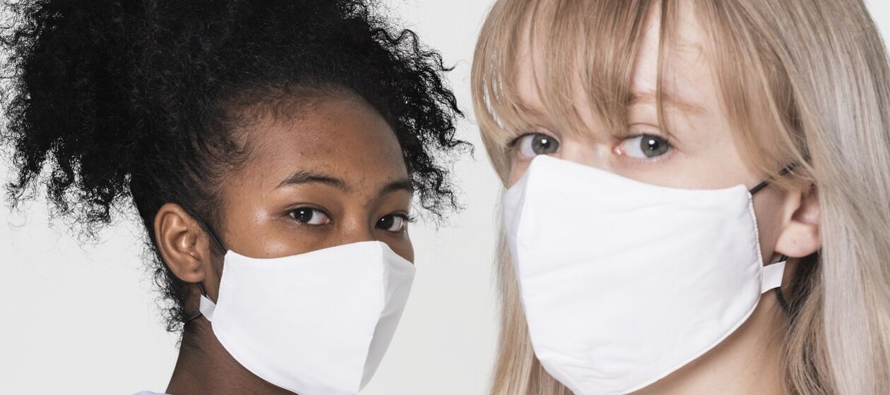 Zwei junge Frauen mit Mund-Nase-Bedeckung schauen in die Kamera