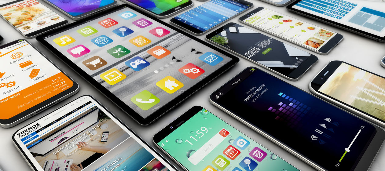 Zahlreiche Tablets und Smartphones liegen nebeneinander auf einem Tisch, bunte Icons und Apps sind zu sehen 