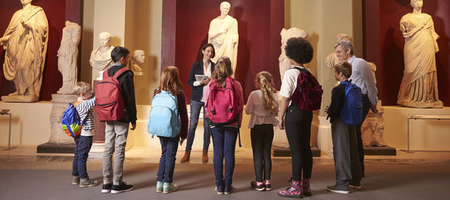 Eine Gruppe von Schülern mit einem Lehrer hört einem Guide im Museum zu.