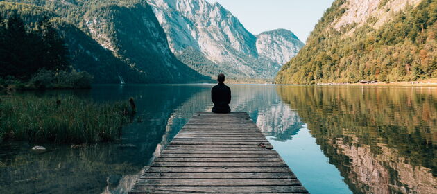 Eine Person sitzt alleine auf einem Steg und schaut auf einen Bergsee