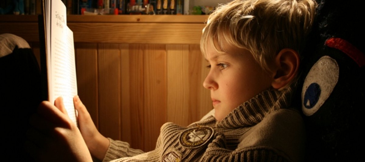 Ein Junge sitzt in Decken und Kissen, um ein Buch zu lesen.