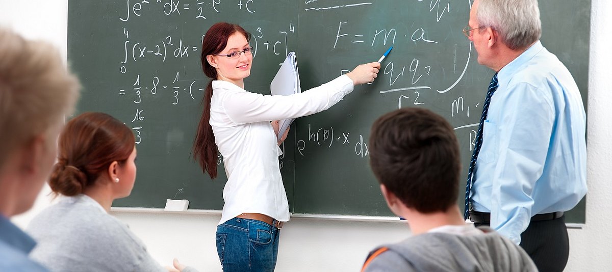 eine Frau erklärt Formeln an einer Tafel