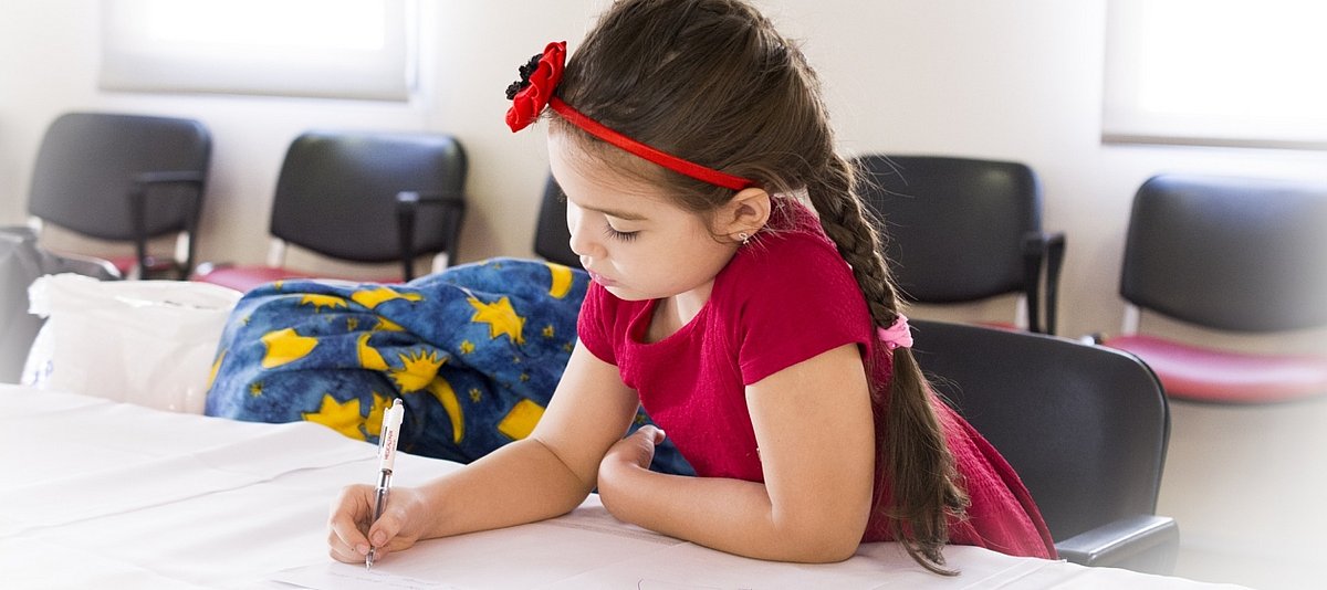 Ein Grundschülmädchen sitzt in der Schule an einem Tisch und schreibt etwas