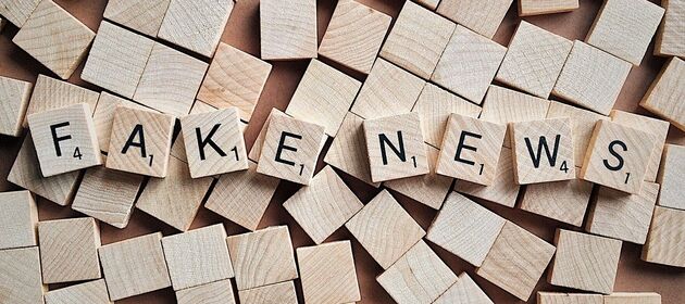 Holzfarbene Scrabble-Steine legen den Begriff "Fake News"