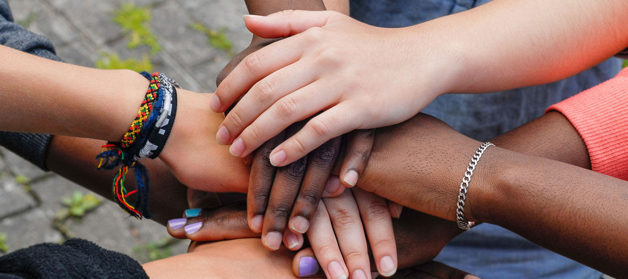 Die Hände von jungen Menschen unterschiedlicher Herkunft, die im Kreis stehen, liegen übereinander. 