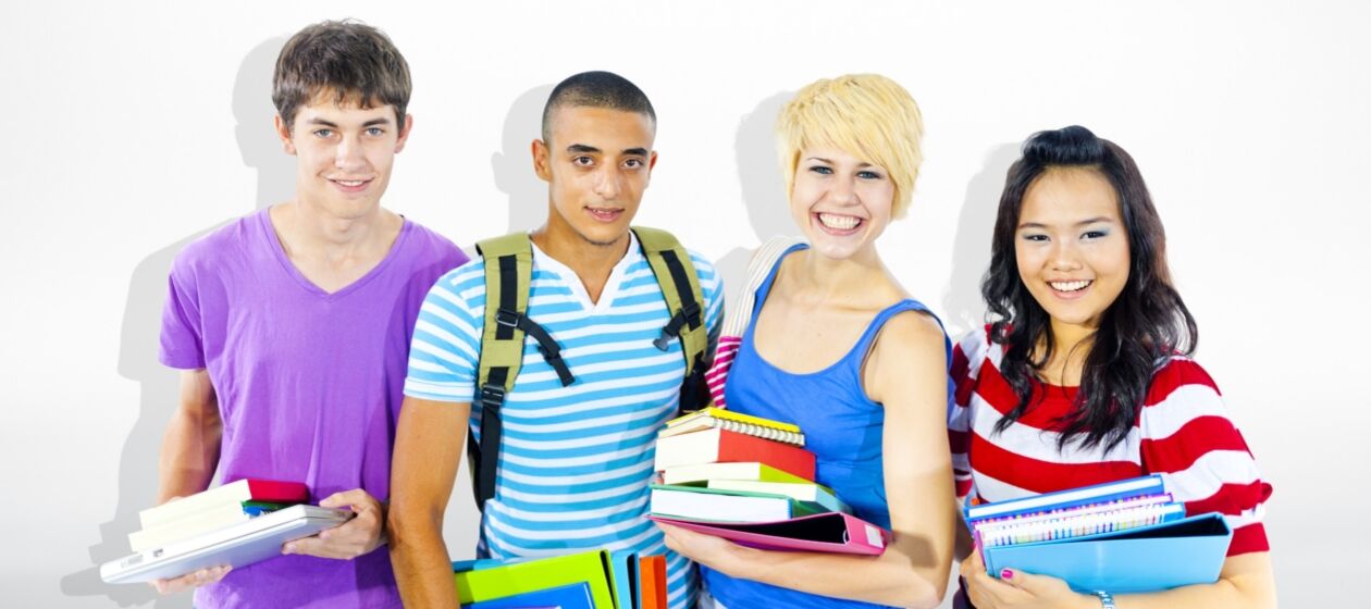 Vier Studierende stehen nebeneinander, tragen Bücher udn Rücksäcke und lachen