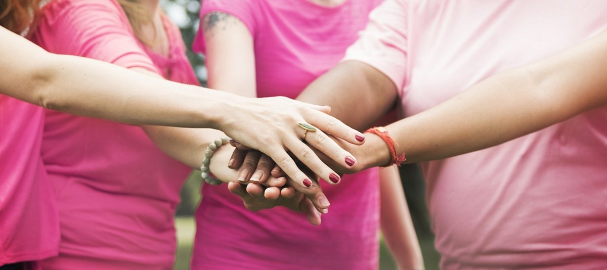 Fünf Mädchen, die in Pink angezogen sind, legen ihre Hände als Teamgeste übereinander