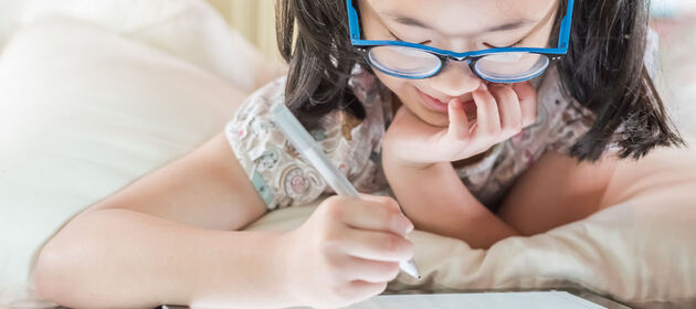 Ein Mädchen im Grundschulalter beschäftigt sich mit einem Stift und einem Tablet.