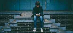 Junge sitzt allein auf einem Treppenabsatz und schaut auf sein Smartphone