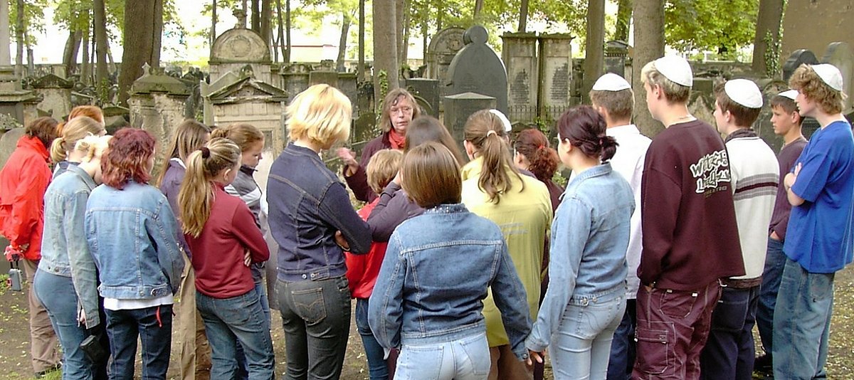 Jugendliche hören einen Vortrag auf einem jüdischen Friedhof