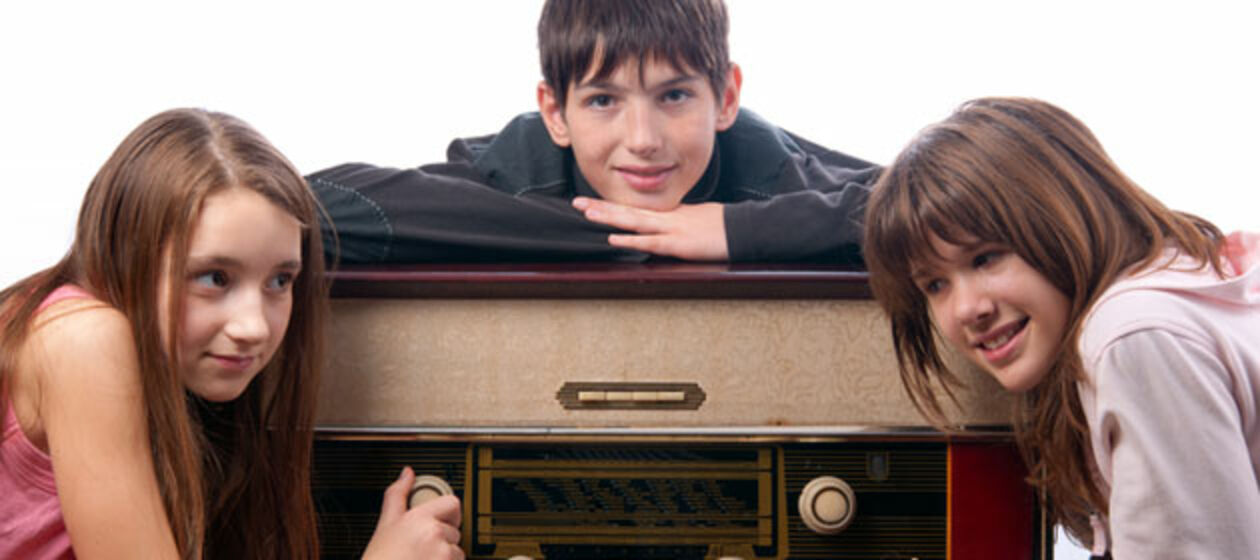Drei Jugendliche gruppieren sich um ein altes Radio