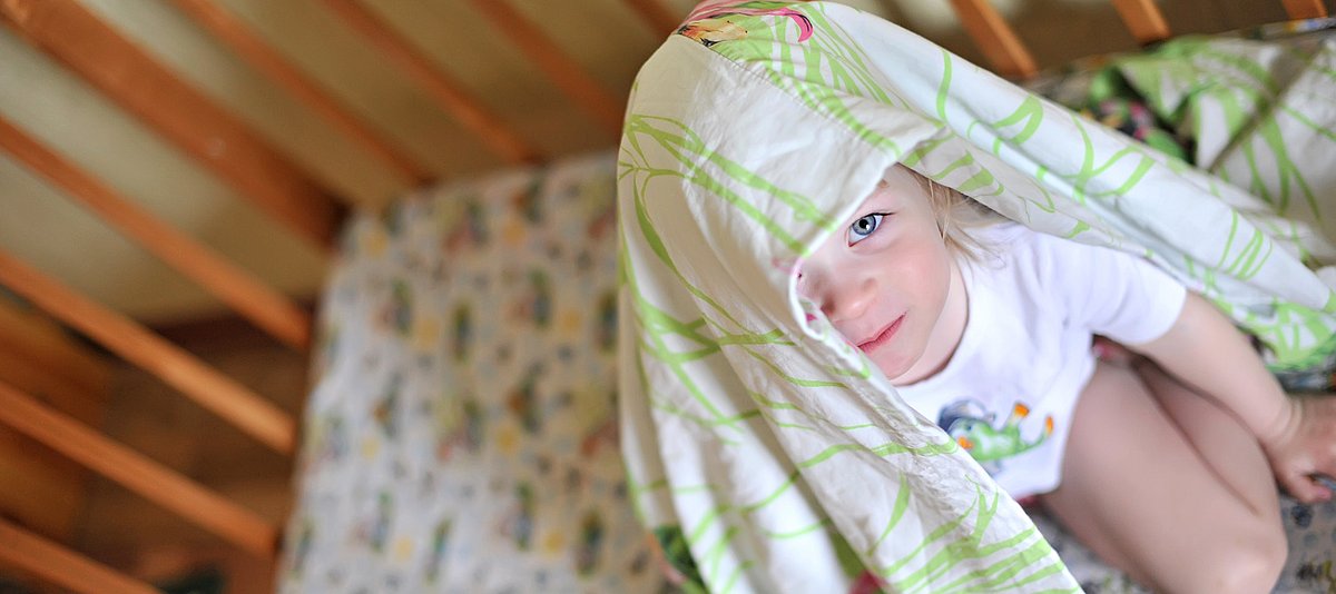 Kind im Bett hat die Decke über den Kopf gezogen