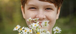 Ein Kind mit Sommersprossen hält einen Blumenstrauß in der Hand