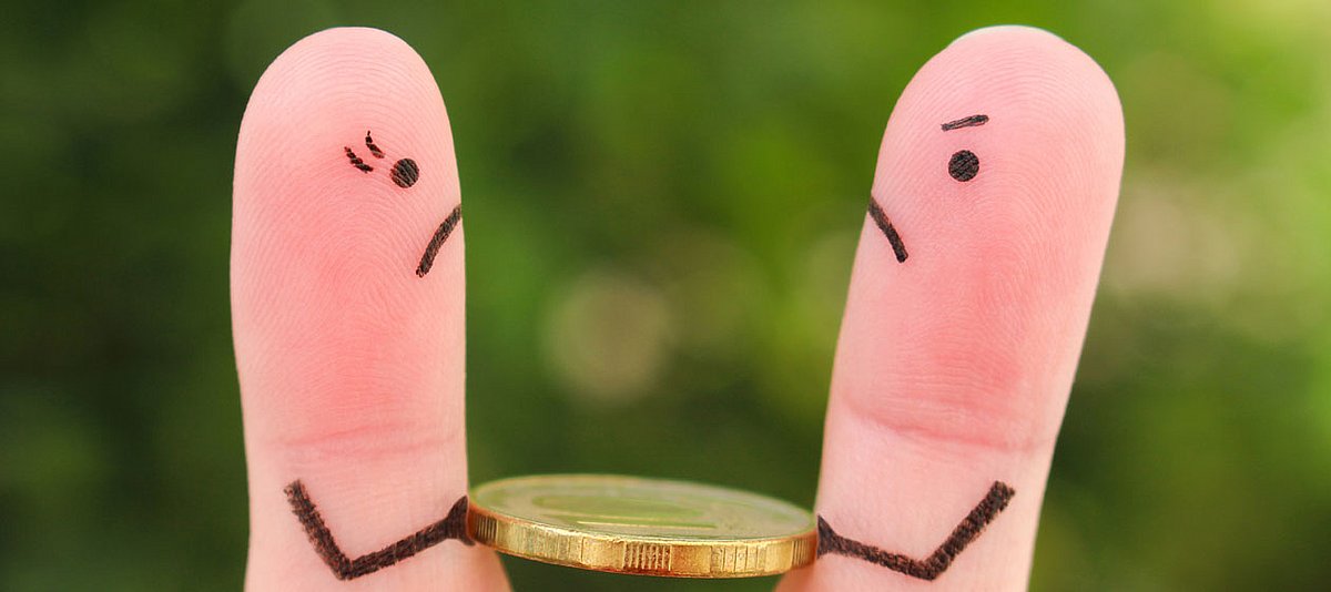 Zwei Finger mit einem gezeichneten, verärgerten Gesicht halten eine Münze.