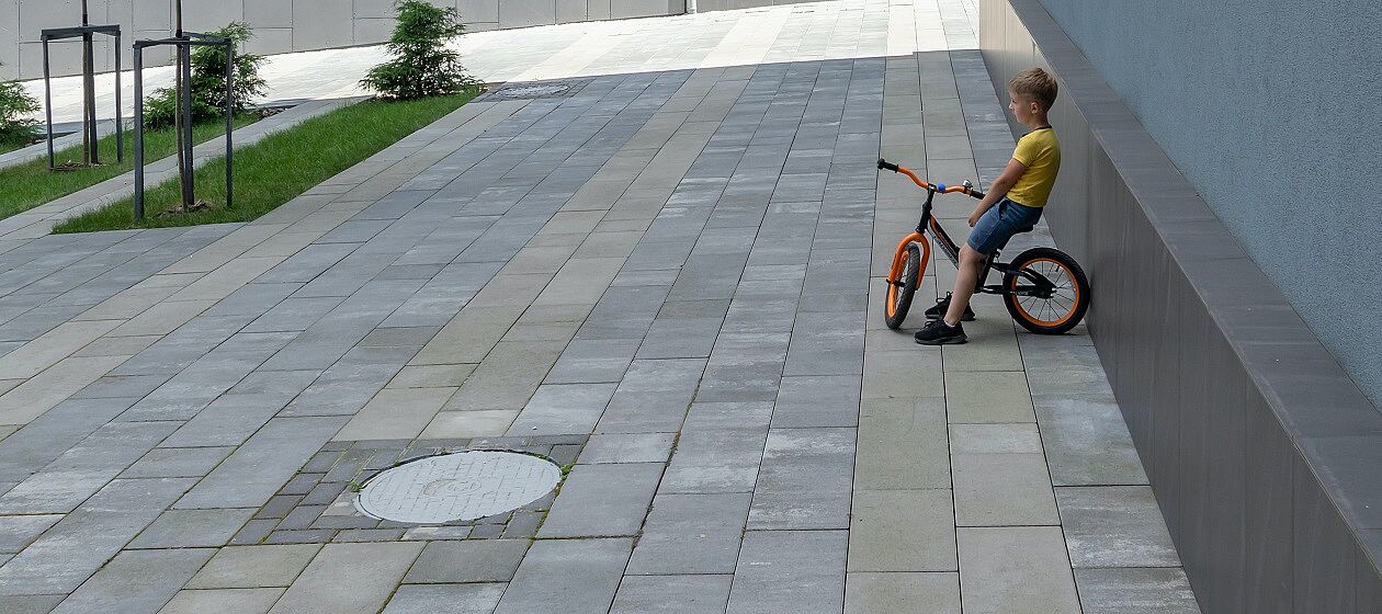 Ein Kind lehnt mit einem Fahrrad an einer Mauer auf einem leeren Platz