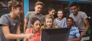 Eine Gruppe Jugendlicher steht und sitzt vor einem Computer
