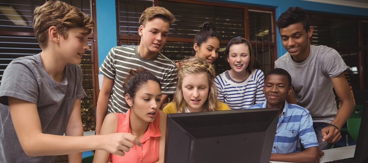 Eine Gruppe Jugendlicher steht und sitzt vor einem Computer