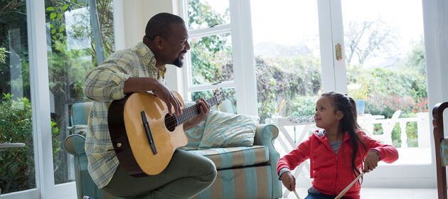 Ein Erwachsener mit einer Gitarre musiziert gemeinsam mit einem Kind 