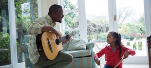 Ein Erwachsener mit einer Gitarre musiziert gemeinsam mit einem Kind 