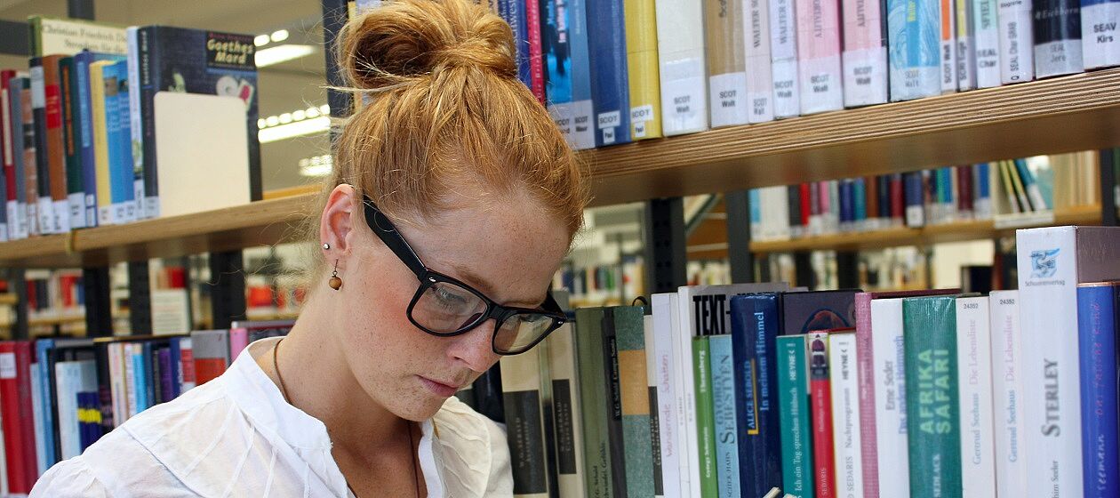 Eine junge Studentin liest in der Bibliothek ein Buch.