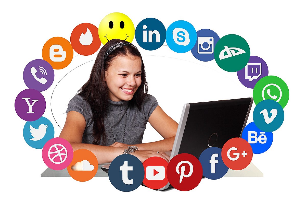 Ein Mädchen sitzt am Laptop und wird von von Social Media-Icons umkreist.