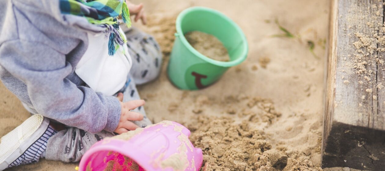 Kleinkind sitzt in Sandkasten und spielt mit Eimern