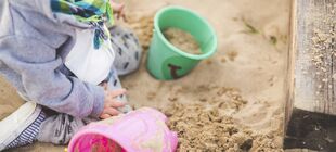 Kleinkind sitzt in Sandkasten und spielt mit Eimern