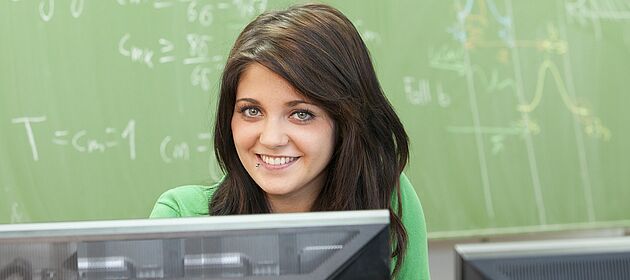 Ein junges Mädchen sitzt vor einer Tafel, auf der mathematische Gleichungen stehen.