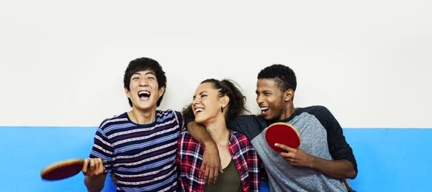 Drei junge Menschen lachen vertraut und haben Tischtennisschläger in der Hand