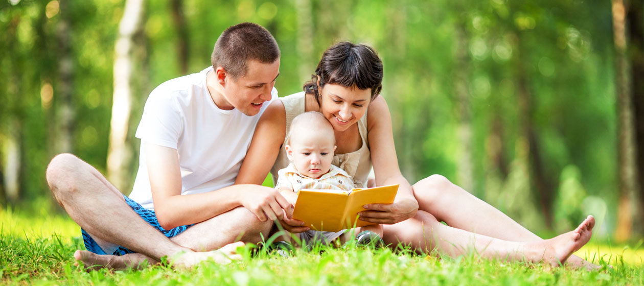 Eine glückliche Familie sitzt im Park und schaut mit dem Baby ein Buch an.