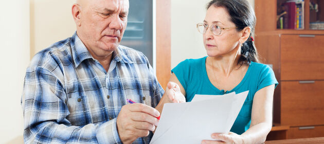 Ein älteres Ehepaar schaut sich besorgt Unterlagen an.