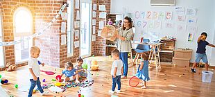 Eine Erzieherin und mehrere Kinder in einem Gruppenraum, von Spielsachen umringt