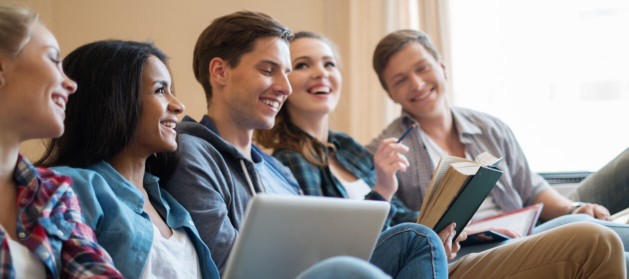 Fünf Jugendliche sitzen zusammen, mit Laptop auf den Beinen und lachen