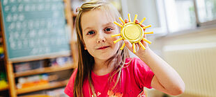 Ein Mädchen hält eine gebastelte Sonne hoch.