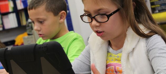Zwei Grundschulkinder sitzen an Tischen und bedienen einen Laptop
